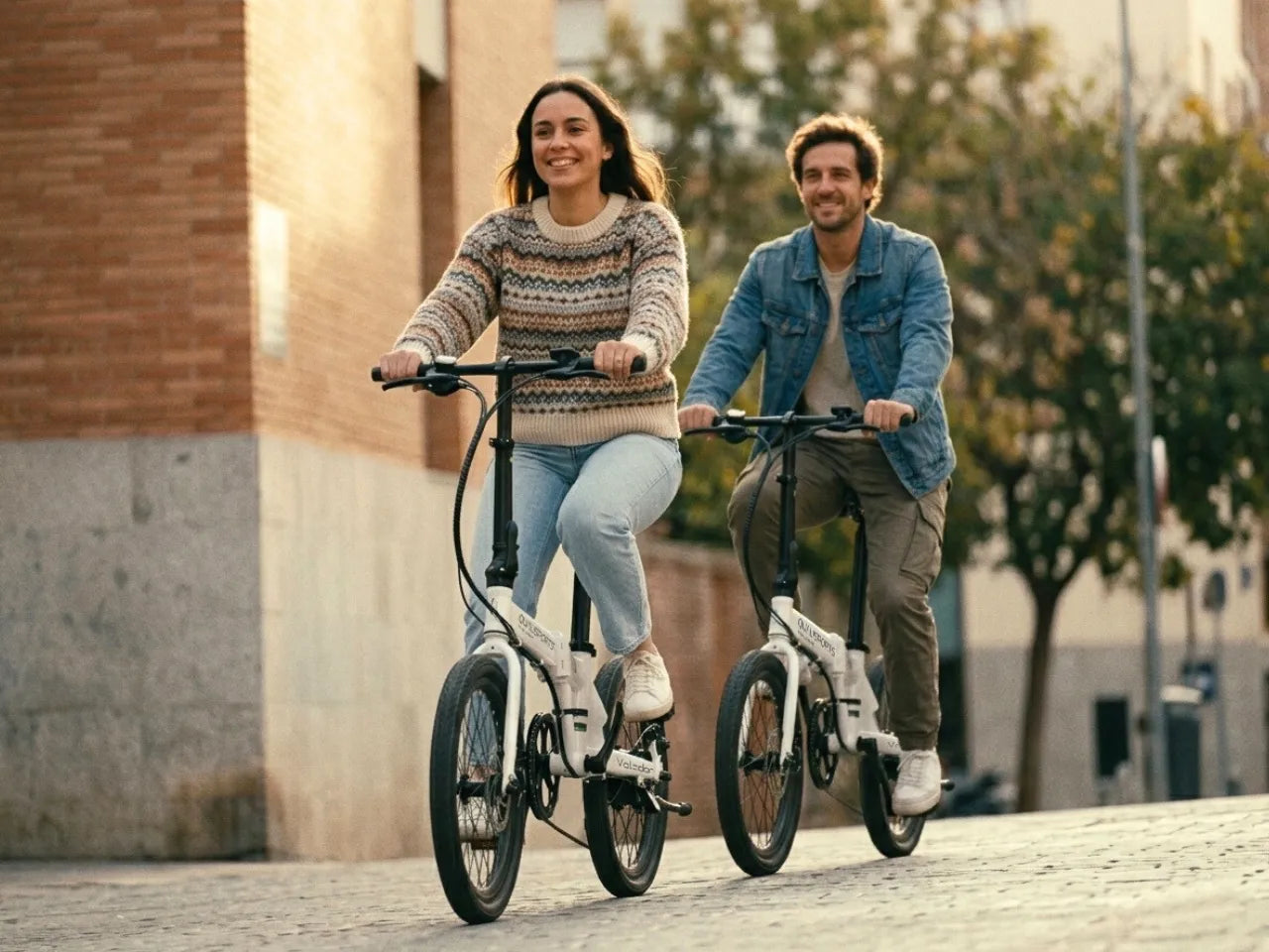 Two people riding compact electric bicycles on a city street.