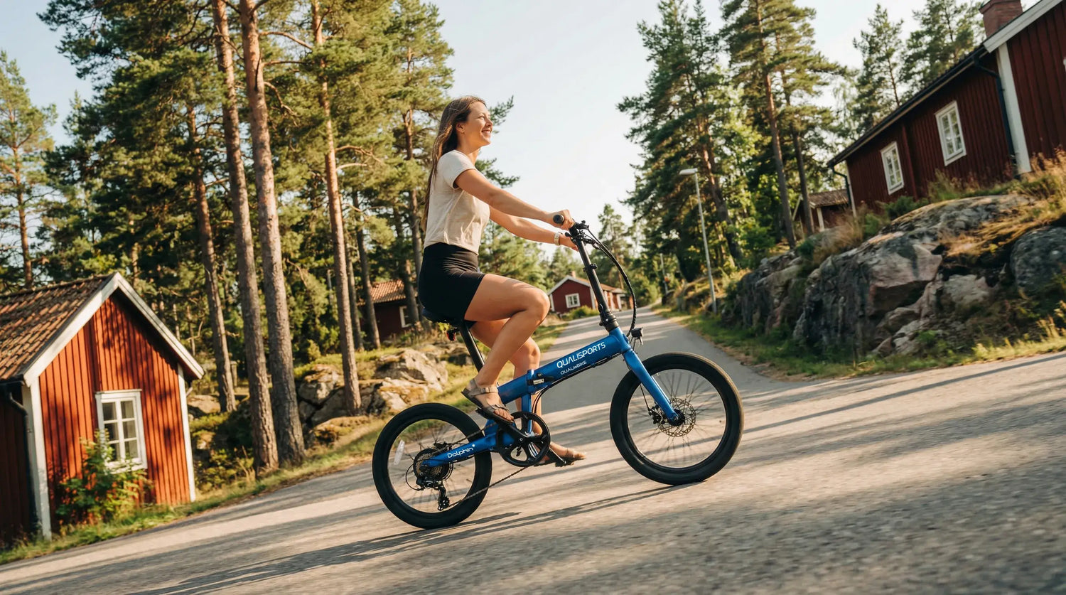 Person riding a blue portable electric bike on a road with trees and a cabin in the background