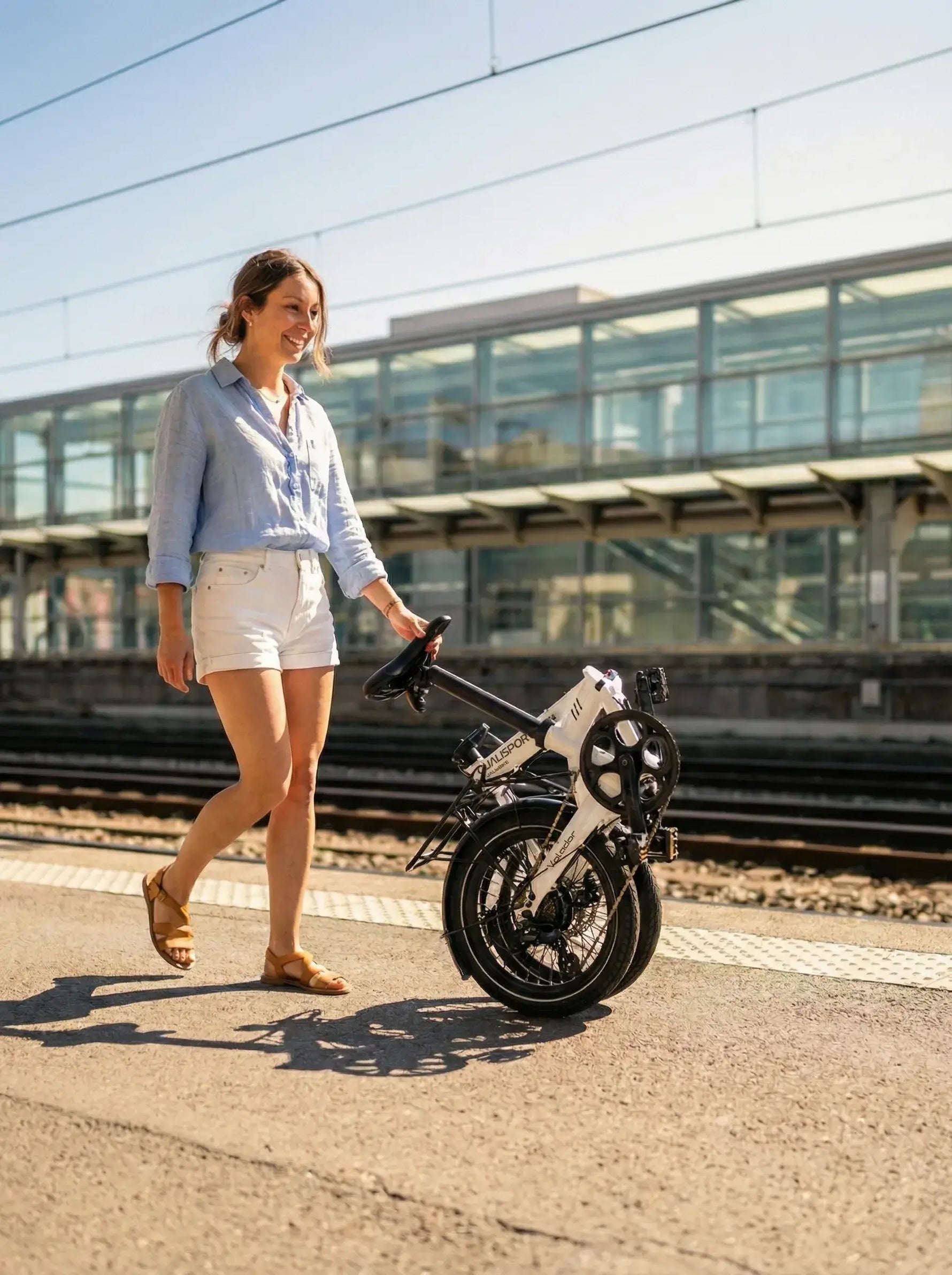 Woman walking with a compact folded electric bike near train tracks