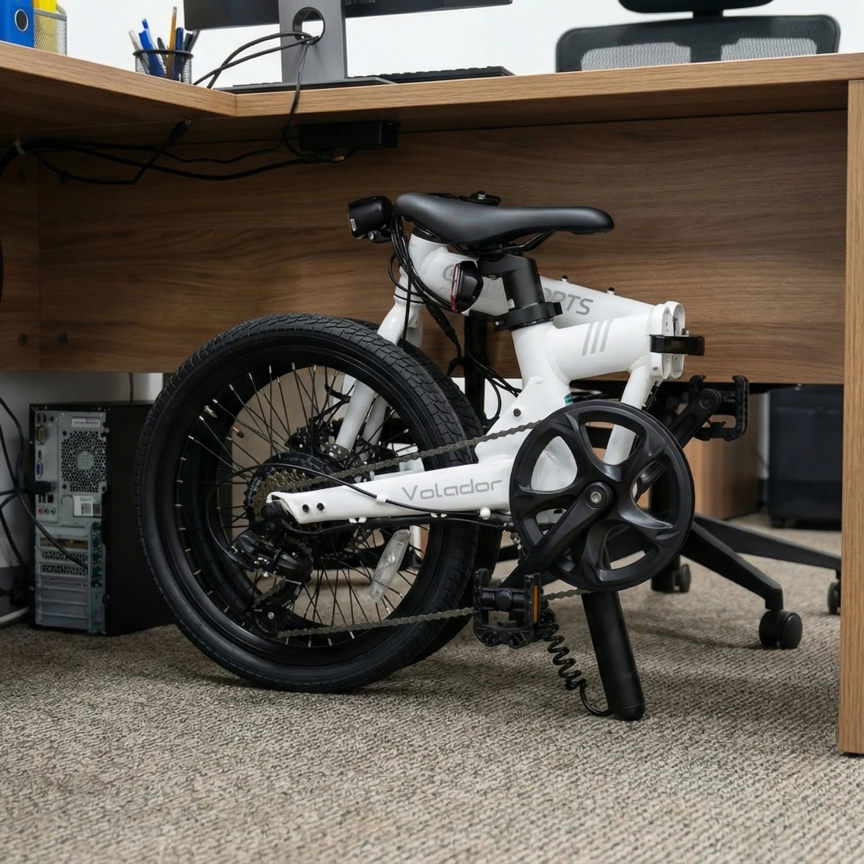 Small white volador electric bike with black components leaning against a wooden desk.